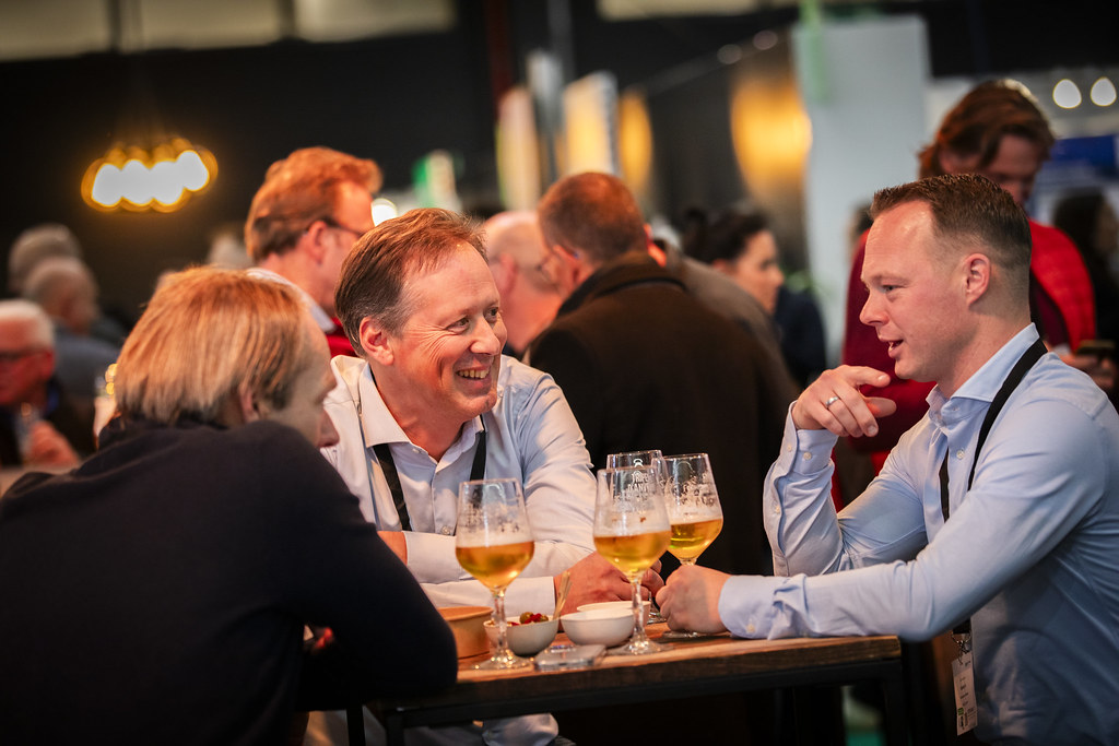 Drie mannen in gesprek aan een statafel met bierglazen op de beursvloer van Solids Antwerpen