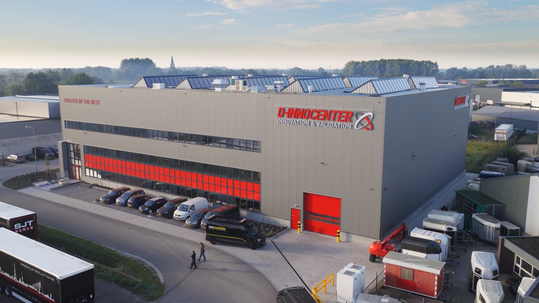 Luchtfoto van het grijze D-Innocenter van Dinnissen in Sevenum met rode raampanelen en het logo D-Innocenter Innovation & Validation op de gevel
