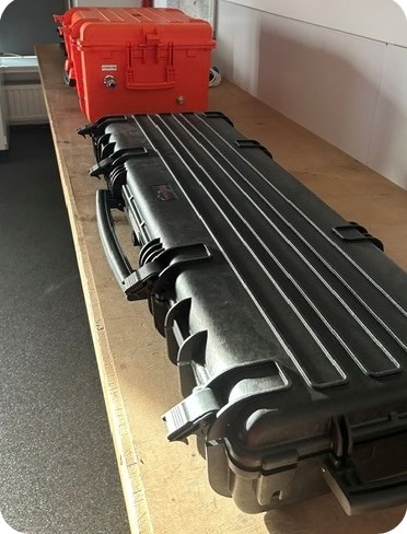 Zwarte transportkoffer voor de meetlans naast een oranje OMK 1.2-koffer